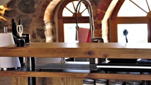 A kitchen with a stone wall, arched windows, a wooden countertop, and a sink with a faucet. - Designer apartment with sauna, hot tub and fireplace (Großharthau)