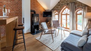 A loft bedroom with a brick wall, a fireplace, a sofa, a TV, and a dining area with stools. - Designer apartment with sauna, hot tub and fireplace (Großharthau)