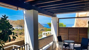 A covered outdoor patio with a glass table, chairs, and a view of the sea.