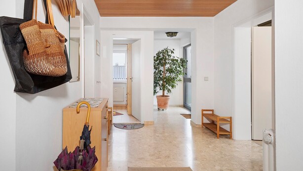 En gang med træloft, en potteplante, en bænk og en dør.