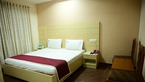 A hotel room with a bed, bedside table, chair, and a curtain. - Hotel pams (Mayiladuthurai)