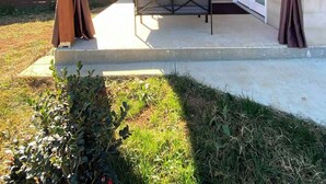 Une terrasse extérieure couverte, équipée d’une table et de chaises, d’un ventilateur de plafond et d’un téléviseur fixé au mur.
