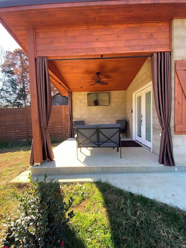 An outdoor covered patio with a table and chairs, a ceiling fan, and a TV mounted on the wall.