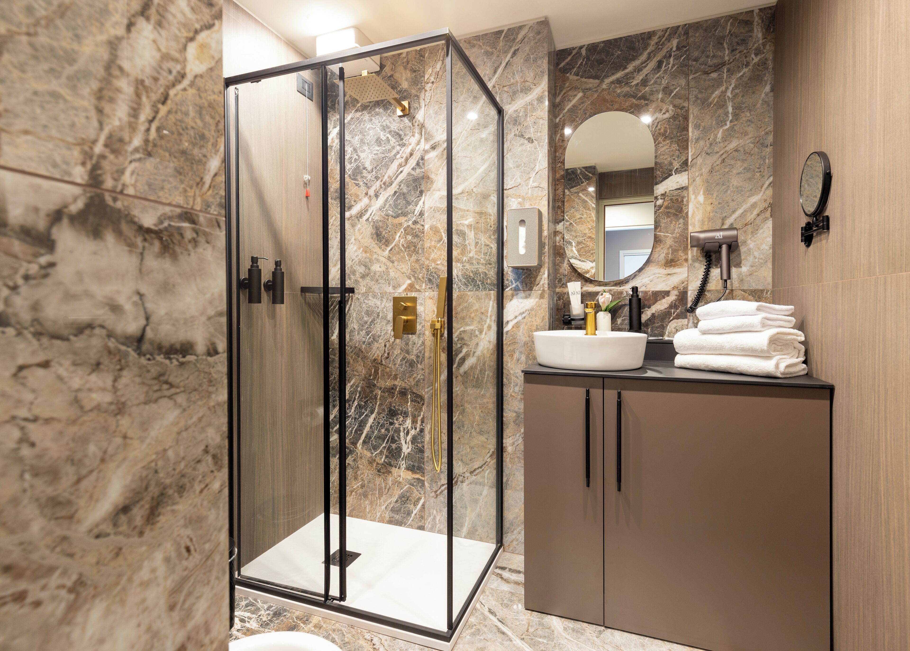 A modern bathroom with a glass-enclosed shower, marble walls, a sink with toiletries, and a mirror.