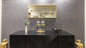 A modern room with a geometric-patterned wall, a black console table with a mirror, and decorative vases. - AH - Collezione Brera (Milan)
