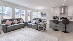 Un salon moderne avec un canapé en cuir gris, un tapis à motifs et un coin repas comprenant une petite table et des chaises.