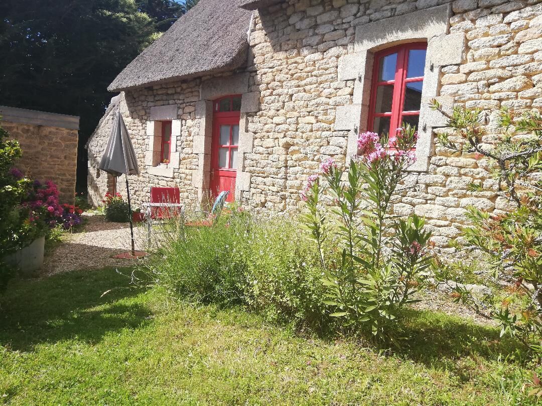A stone house with red doors and windows, surrounded by greenery and a garden.