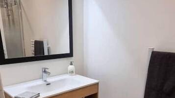 A small bathroom with a wooden vanity, a mirror, a white sink, and a black towel hanging on the wall.