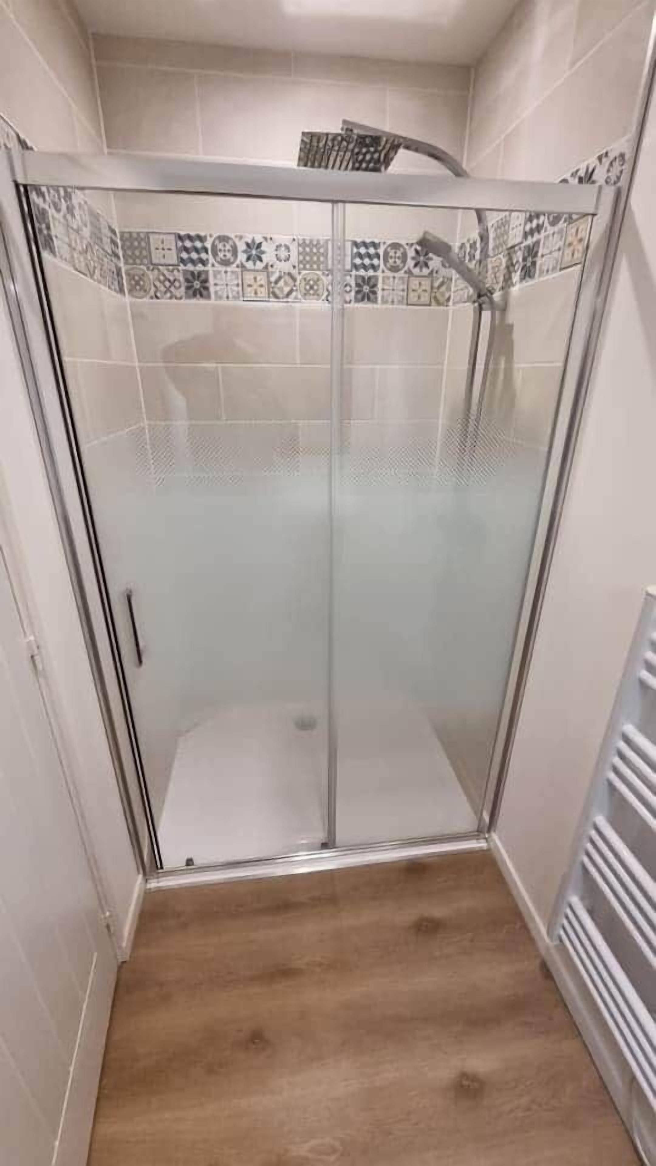 A glass-enclosed shower with a tiled backsplash and a wooden floor.