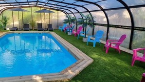 A pool area with a glass enclosure, surrounded by colorful chairs and a wooden deck. - Chalet 7 - 8P-Pool -100m Black Frame (Saumur)