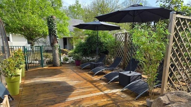 A wooden deck with outdoor seating and umbrellas, surrounded by greenery and a fence. - Chalet 7 - 8P-Pool -100m Black Frame (Saumur)