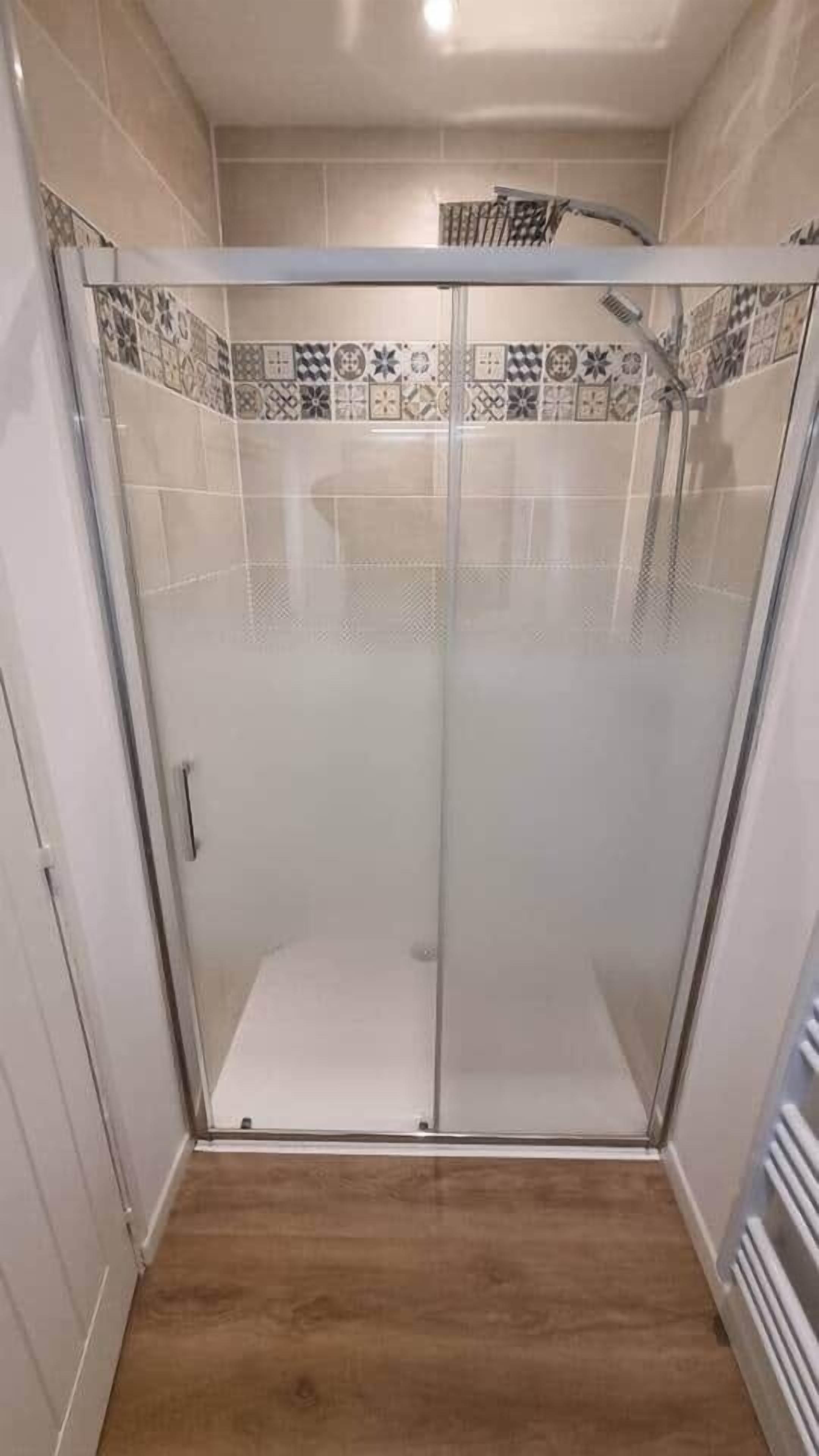 Una ducha a ras de suelo con puerta de cristal, paredes de azulejos y suelo de madera.