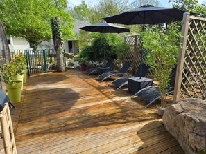Eine Holzterrasse mit Sitzgelegenheiten und Sonnenschirmen, umgeben von Grünpflanzen und einem Zaun.