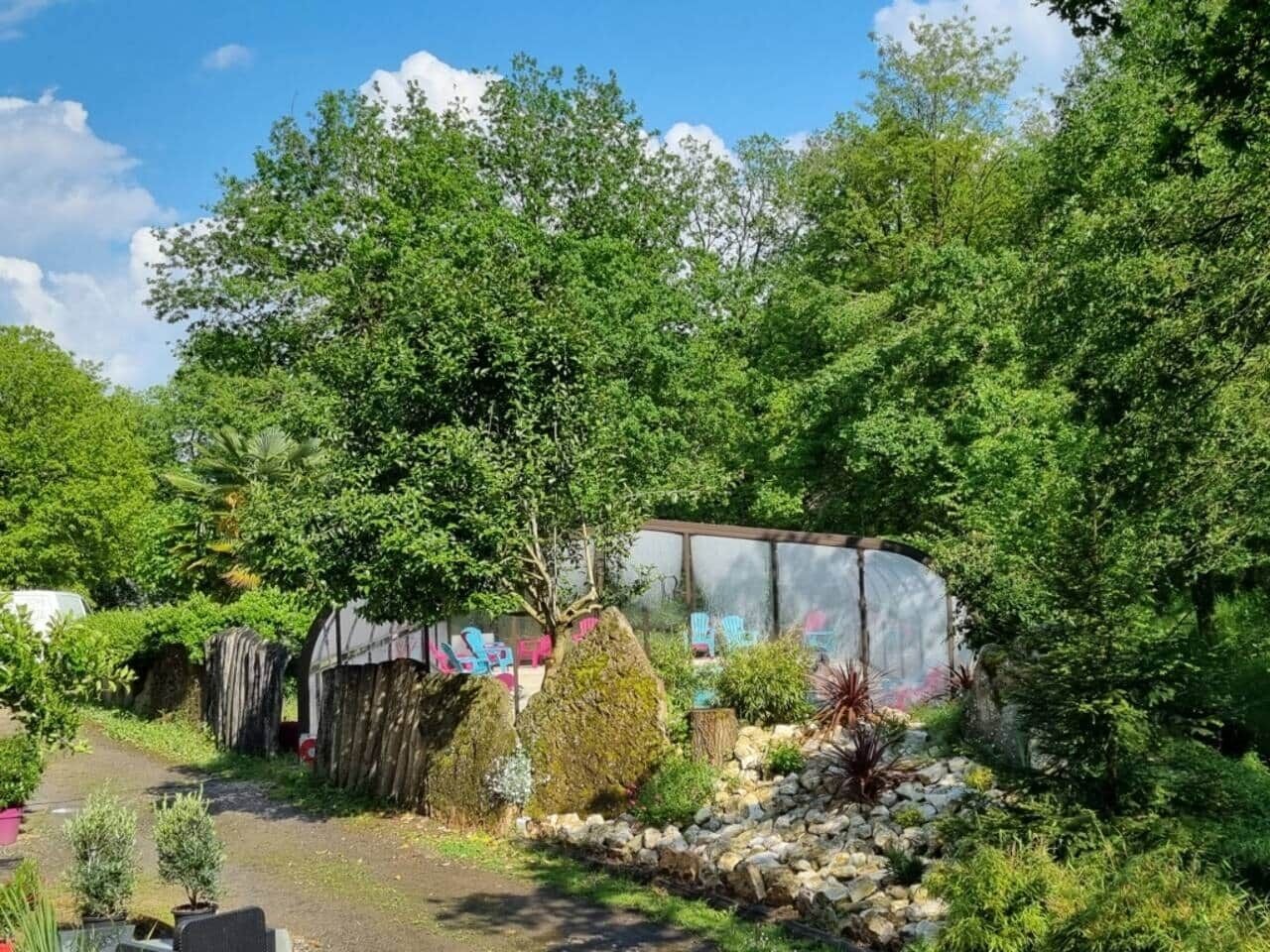 A greenhouse with a glass roof, surrounded by lush greenery and a variety of plants.