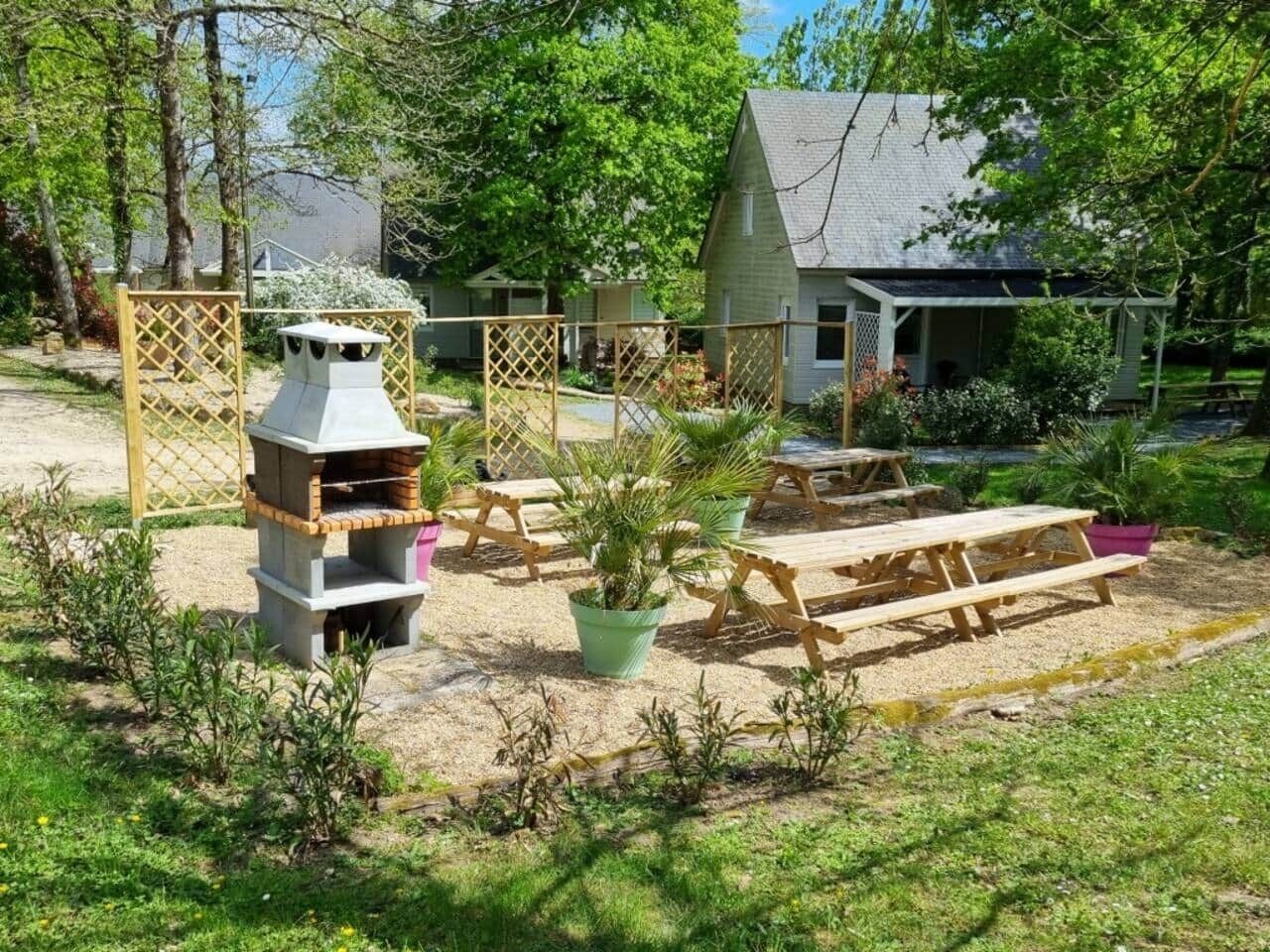 Un jardin avec un barbecue, des tables de pique-nique et une maison en arrière-plan.