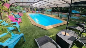 A covered outdoor swimming pool with artificial grass, surrounded by blue and pink lounge chairs. - Suite S2 - Pool & Park, 100m Cadre Noir (Saumur)