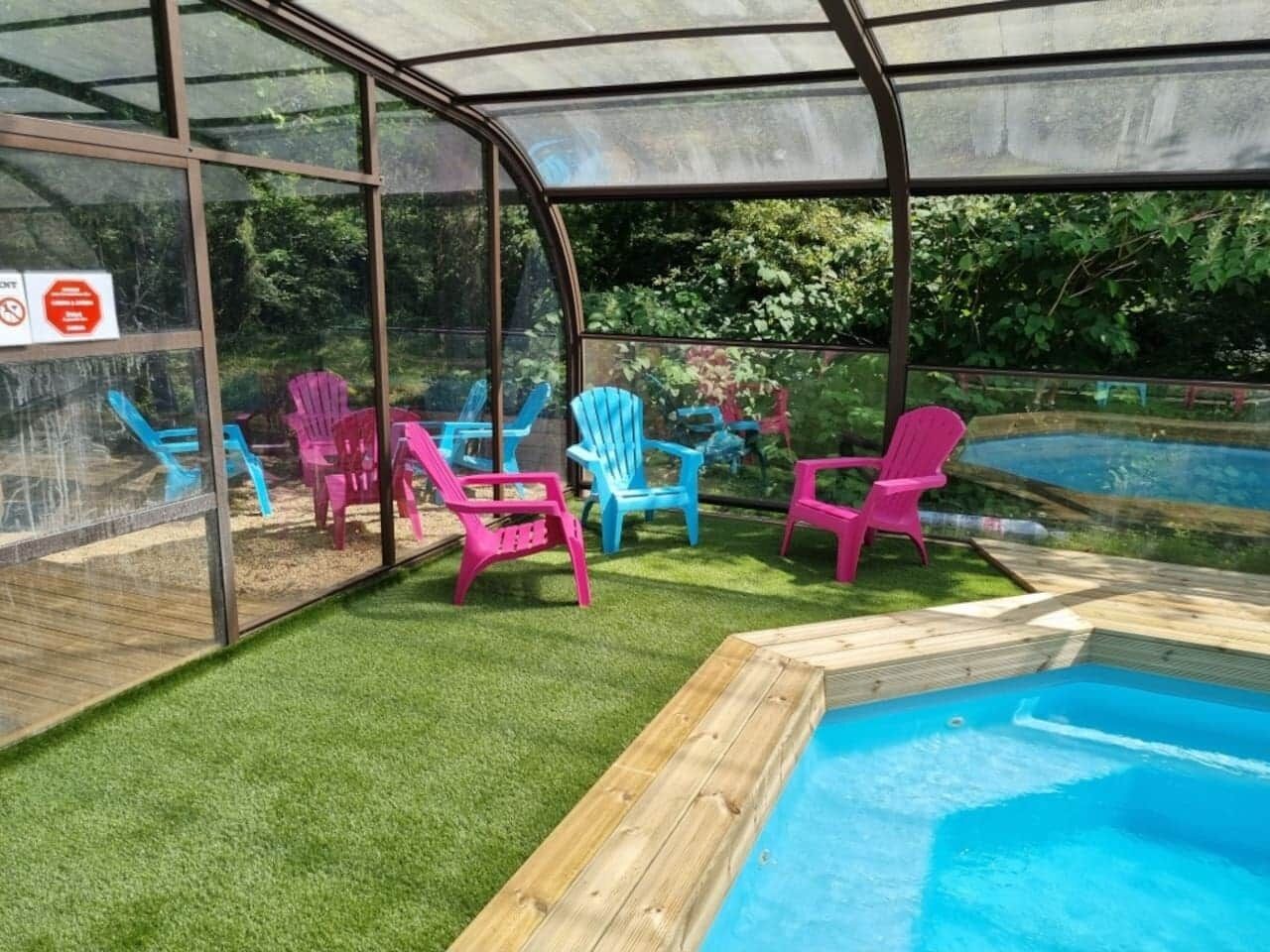 Ein überdachter Außenbereich mit Pool, grünem Kunstrasen und bunten Plastikstühlen.