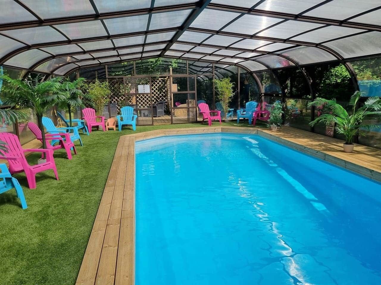 Una piscina techada con un deck de madera y sillas de colores.