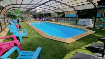 Ein überdachter Pool mit Kunstgrasanlage und Liegestühlen.