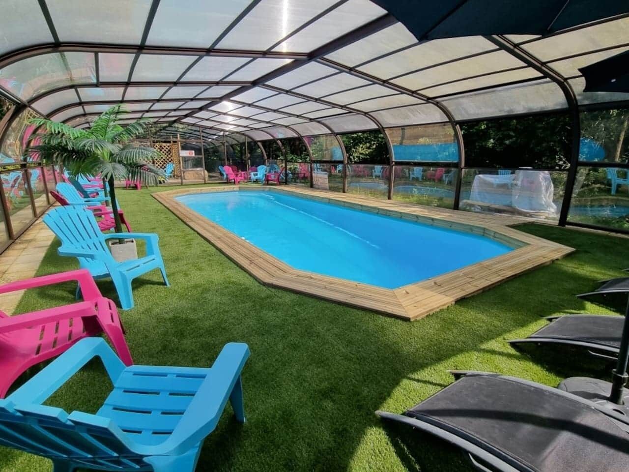 A covered swimming pool with artificial grass and lounge chairs.