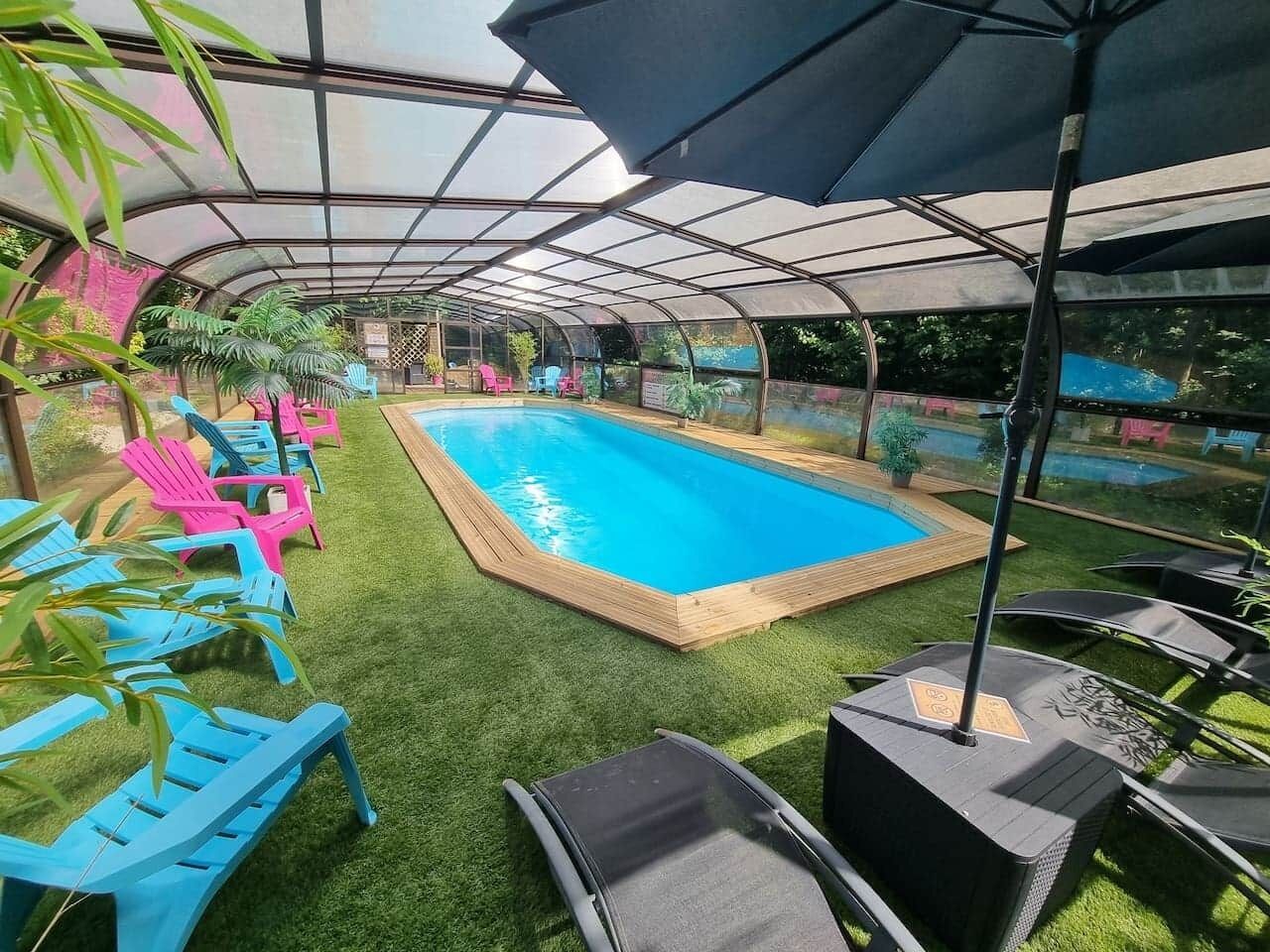 A covered outdoor swimming pool with artificial grass, surrounded by blue and pink lounge chairs, and a canopy overhead.