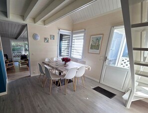 A dining area with a table and chairs, a window with blinds, and a door leading outside. - Chalet 8 - 8P - Piscine & Parc , 100m Cadre Noir (Saumur)