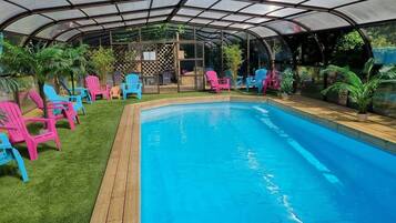A covered swimming pool with colorful chairs and potted plants.