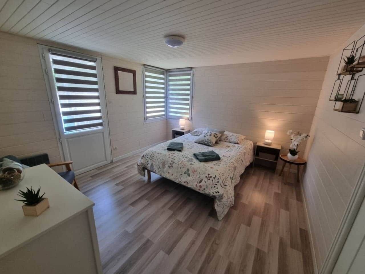 A bedroom with a bed, bedside tables, a desk, and a window with blinds.
