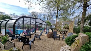 Un área de estar al aire libre techada con sillas Adirondack, una piscina y una estructura tipo invernadero.