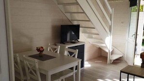 Un comedor con una mesa y sillas, un televisor sobre un mueble bajo y una escalera que sube a un nivel superior.