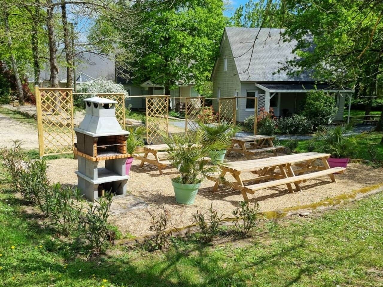 Een achtertuin met een barbecue, picknicktafels en een huis op de achtergrond.