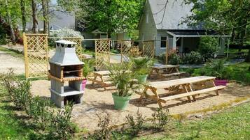 Een achtertuin met een barbecue, picknicktafels en een huis op de achtergrond.