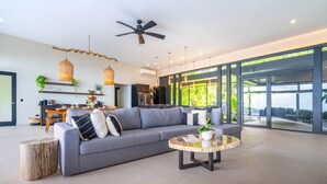A modern living room with a grey sofa, a round coffee table, and a ceiling fan. - Jungle Luxury Villa • 3BR w/ Pool & Ocean View (Savegre)