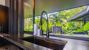 A modern kitchen with a black countertop, stainless steel sink, and a window overlooking a lush garden. - Jungle Luxury Villa • 3BR w/ Pool & Ocean View (Savegre)