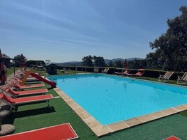 Piscina con tobogán, tumbonas y vistas a montañas.