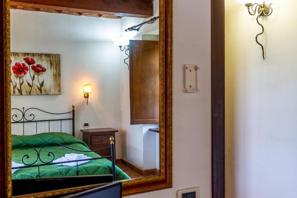 A bedroom with a green bed, a wooden nightstand, a wall-mounted lamp, and a painting of red flowers.