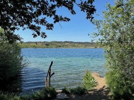 Una vista despejada de un lago con un sendero que llega hasta la orilla, rodeado de vegetación y colinas al fondo.