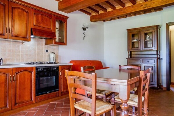 A kitchen with wooden cabinets, a dining table with chairs, a built-in oven, and a cabinet with glass doors. - Alma del Lago Charming Apartments (La Pesta)