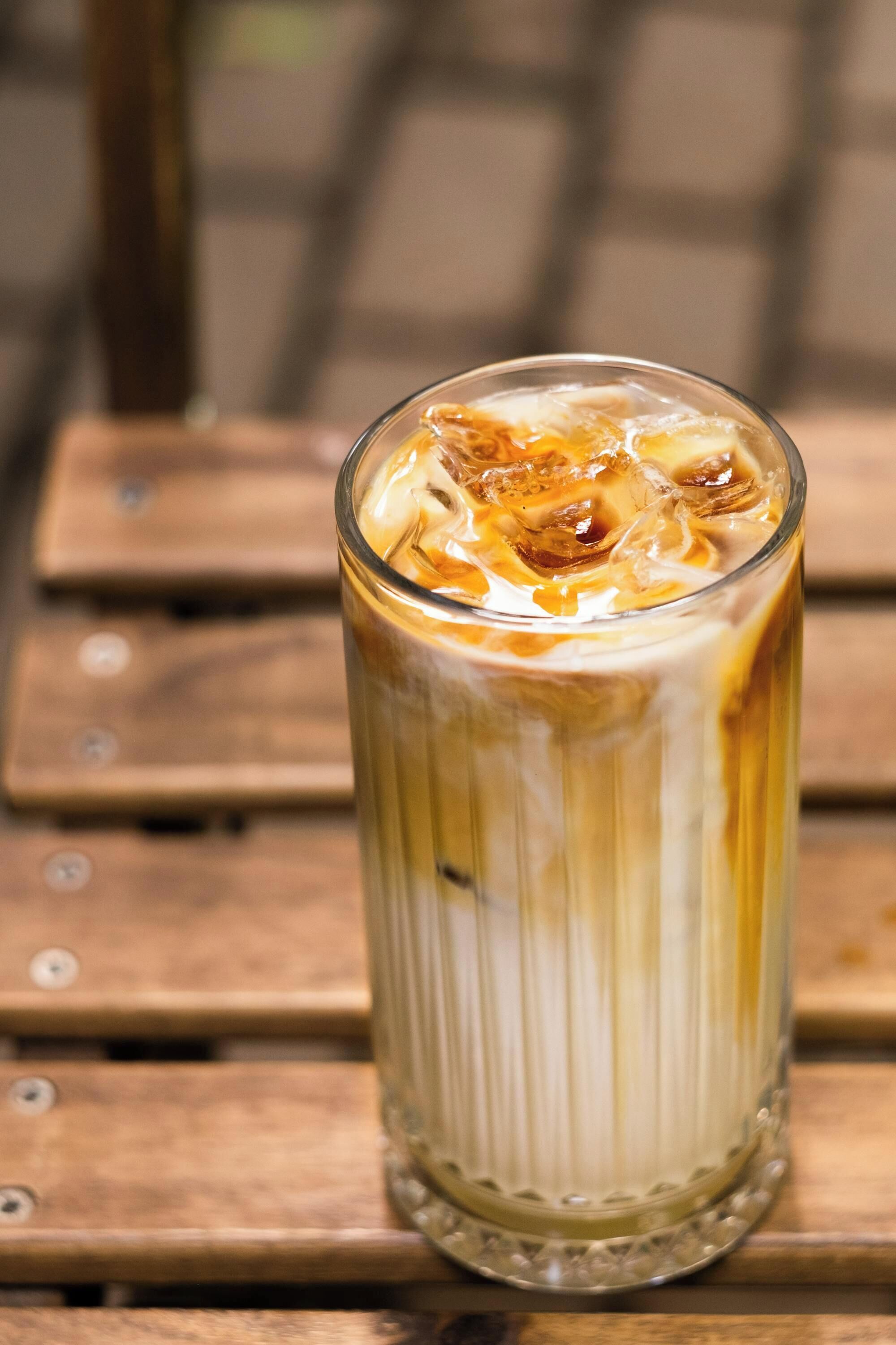 A tall glass of iced coffee with ice cubes on a wooden table.