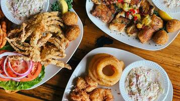 Una mesa de madera con tres platos de mariscos fritos, incluyendo camarones y calamares, acompañados de gajos de limón y ensalada.