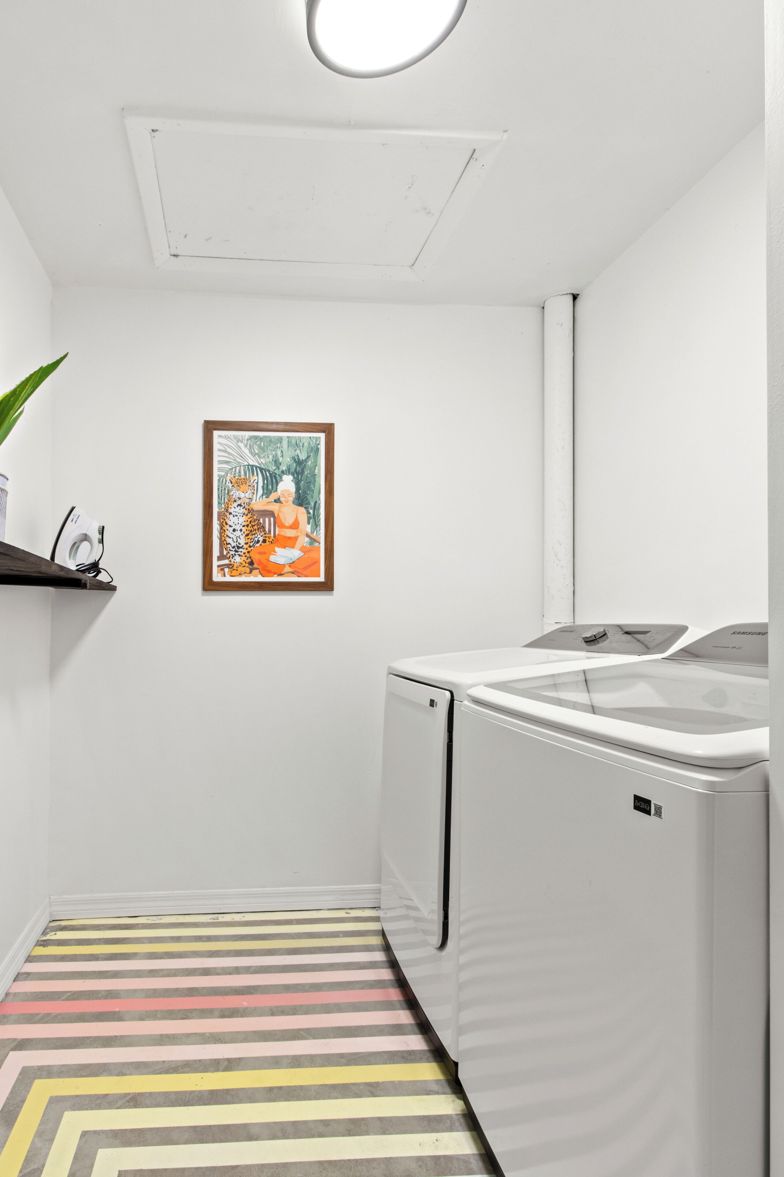 Ein Waschraum mit einer weißen Waschmaschine, einem farbenfrohen Streifenboden und einem gerahmten Bild an der Wand.