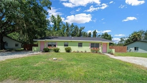 A single-story house with a green exterior and a red door, surrounded by a well-maintained lawn and trees. - Pet-Friendly Crystal River Retreat - Near Manatees & Golf (Crystal River)