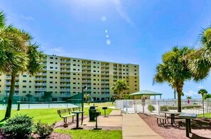 A multi-story hotel with a flat facade, outdoor seating area with benches, and palm trees.