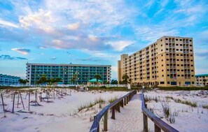 A beachfront hotel with a boardwalk leading to the beach, a large building with multiple floors, and a clear sky.