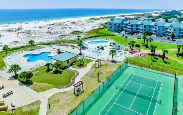 A resort with multiple swimming pools, a tennis court, and a beach view.