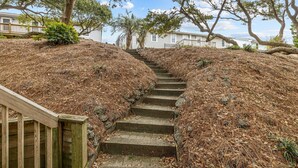 Un escalier en pierre menant au sommet d’une colline, entouré d’aiguilles de pin sèches et bordé d’une rambarde en bois d’un côté.