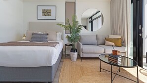 A modern hotel room with a bed, a sofa, a coffee table, a potted plant, and a mirror. - The York | Light + Spacious CBD Apartment (Cape Town)