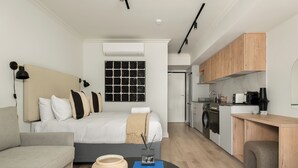 A modern bedroom with a bed, bedside table, and a small TV. The room has a kitchenette with a stove and sink. - Stylish Apartment at The York | Gym (Cape Town)