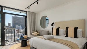 A modern hotel room with a large bed, a round mirror, a small table, and a view of the city through a large window. - Stylish Apartment at The York | Gym (Cape Town)