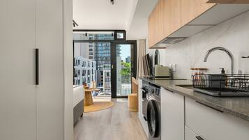 A modern kitchen with a built-in washer and dryer, wooden cabinets, and a large window offering a city view.
